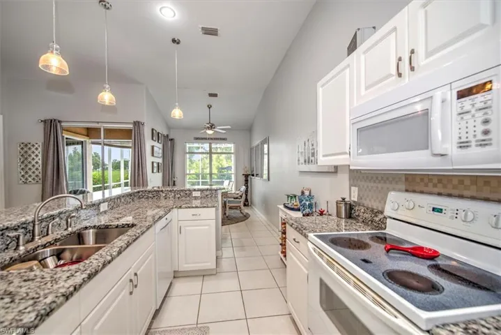 Kitchen with hanging light fixtures, white appliances, white cabinets, sink, and ceiling fan