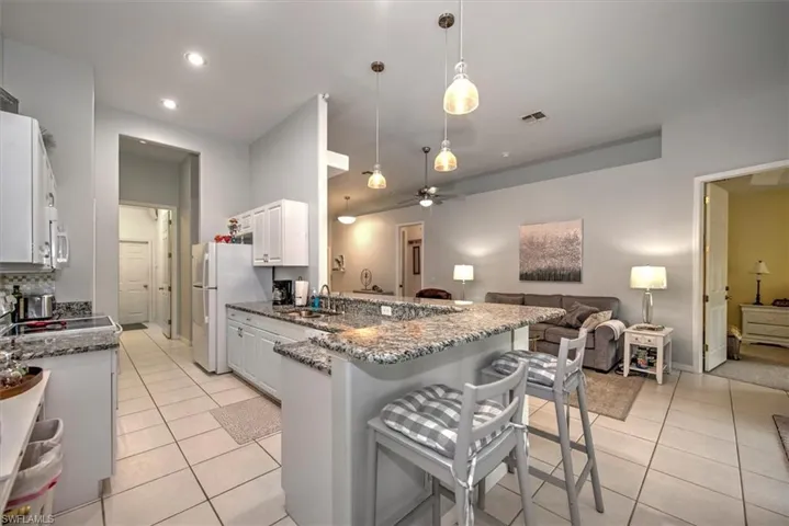 Kitchen featuring white cabinets, stone countertops, a breakfast bar, ceiling fan, and light tile floors