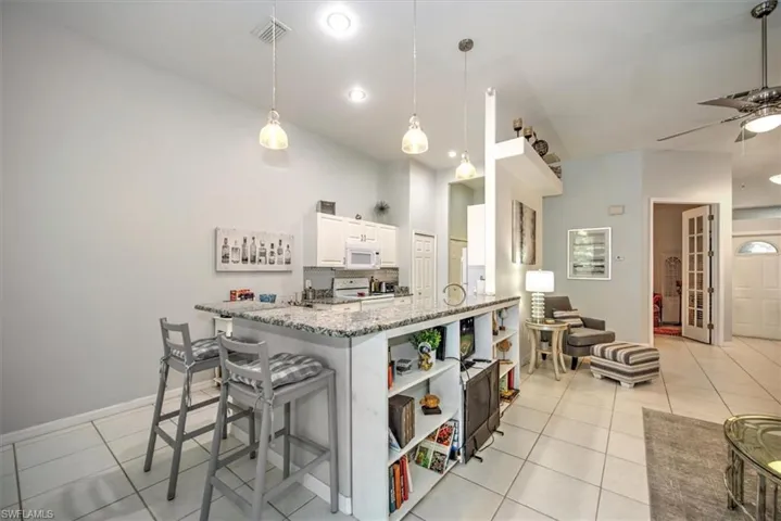 Kitchen with hanging light fixtures, white cabinets, light stone counters, ceiling fan, and light tile floors