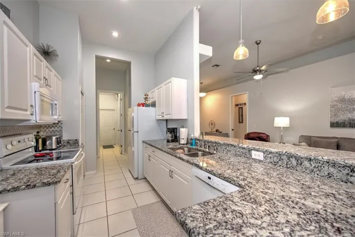 Kitchen featuring white cabinetry, hanging light fixtures, white appliances, sink, and light tile flooring