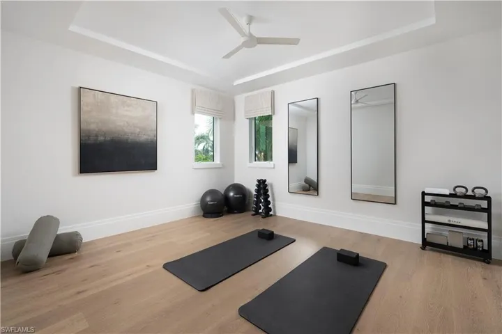 Exercise area with a raised ceiling, ceiling fan, and wood finished floors
