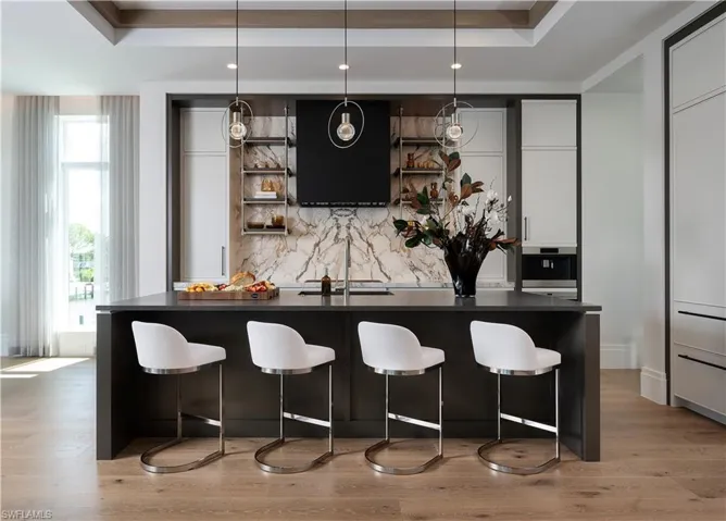 Bar area featuring a raised ceiling, tasteful backsplash, extractor fan, stainless steel oven, and light wood finished floors