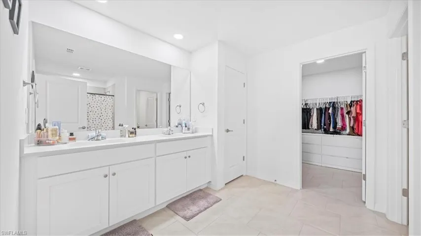 Full bathroom featuring double vanity, curtained shower, a walk in closet, recessed lighting, and light tile patterned floors