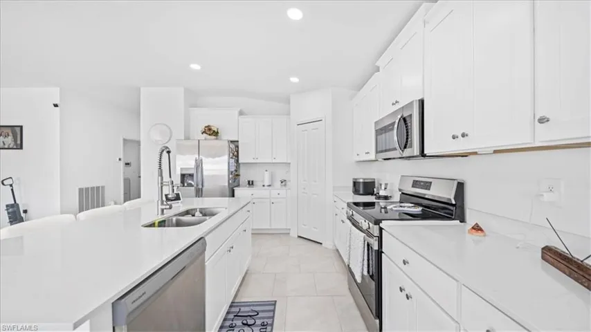 Kitchen with stainless steel appliances, white cabinetry, light stone counters, a kitchen island with sink, and recessed lighting
