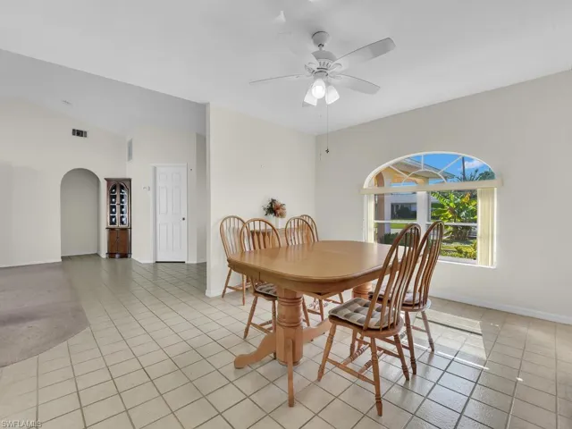Dining room with light tile patterned floors, arched walkways, lofted ceiling, and a ceiling fan
