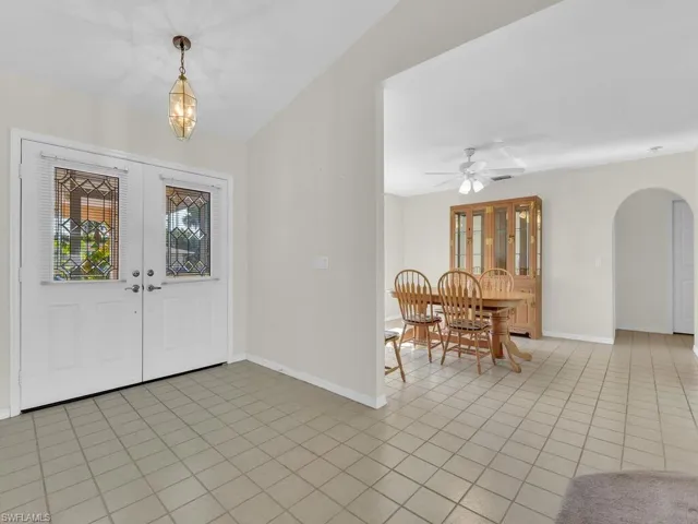 Foyer entrance with arched walkways, light tile patterned floors, french doors, a chandelier, and a ceiling fan