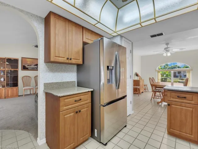 Kitchen with stainless steel fridge, arched walkways, ceiling fan, light stone counters, and light colored carpet