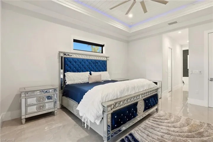 Bedroom with a tray ceiling, ceiling fan, light marble finish floors, and recessed lighting