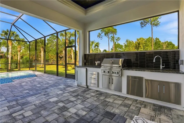 View of patio with exterior kitchen, glass enclosure, a sunroom, and a pool with connected hot tub