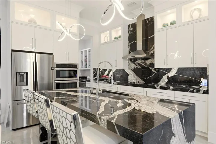 Kitchen featuring glass insert cabinets, dark stone counters, stainless steel appliances, a kitchen breakfast bar, and white cabinetry