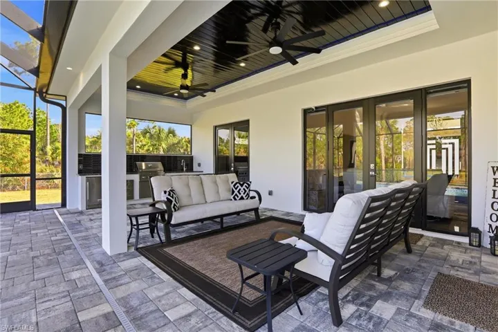 View of patio featuring an outdoor kitchen with living area, glass enclosure, a ceiling fan, and a sunroom