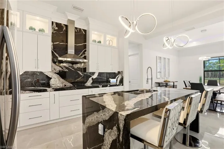Kitchen with dark stone counters, tasteful backsplash, white cabinetry, stainless steel fridge, and range hood