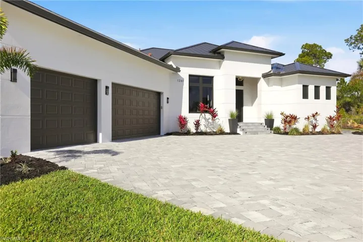 Prairie-style house featuring a standing seam roof, stucco siding, and decorative driveway