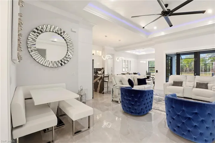 Living room featuring a raised ceiling, ornamental molding, ceiling fan, recessed lighting, and light marble finish floors