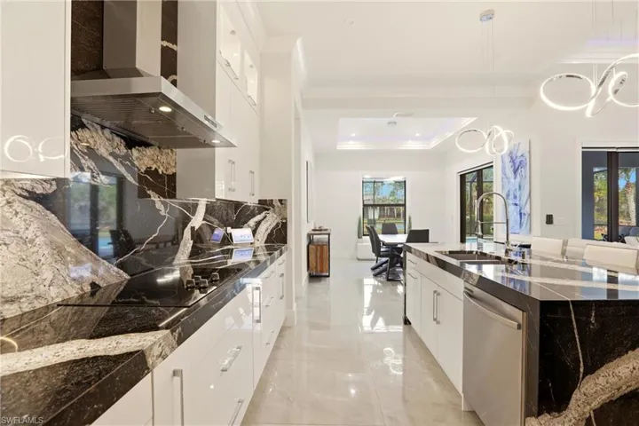 Kitchen with white cabinetry, dark stone countertops, pendant lighting, dishwasher, and a raised ceiling