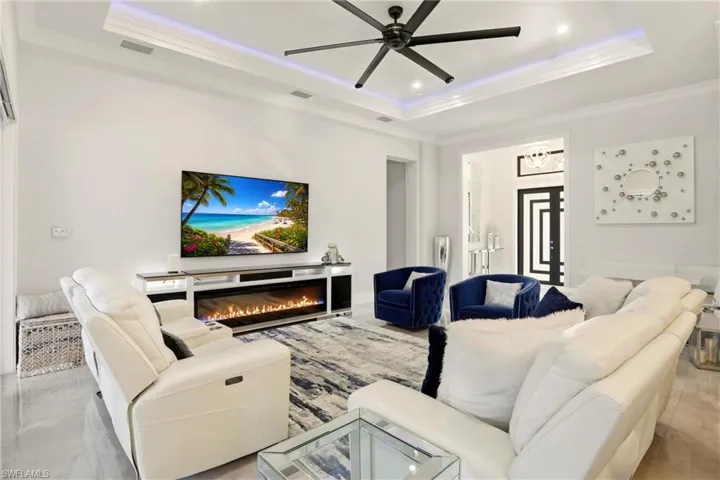 Living room with a ceiling fan, ornamental molding, a glass covered fireplace, a tray ceiling, and recessed lighting