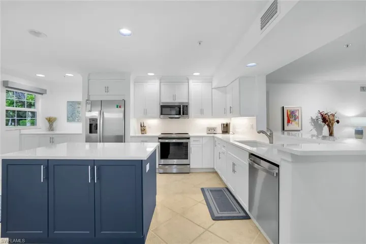 Kitchen with white cabinetry, blue cabinets, appliances with stainless steel finishes, light stone countertops, and recessed lighting
