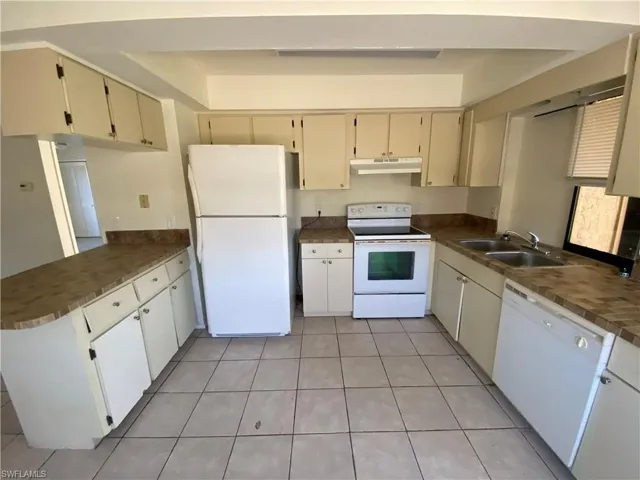 Kitchen featuring white appliances, dark countertops, a peninsula, and light tile patterned flooring