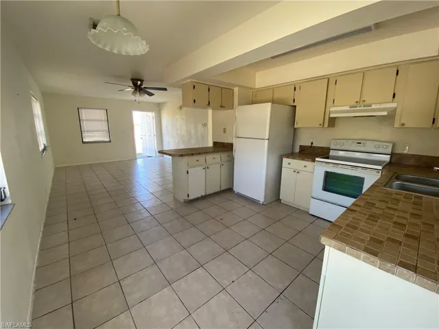 Kitchen featuring white appliances, light tile patterned flooring, a peninsula, tile countertops, and a ceiling fan