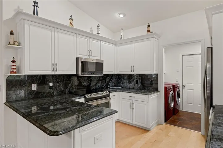 Kitchen with appliances with stainless steel finishes, washing machine and clothes dryer, white cabinets, light hardwood / wood-style floors, and lofted ceiling