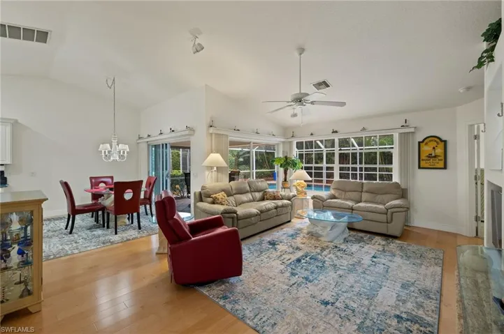Living room with ceiling fan with notable chandelier, light hardwood / wood-style flooring, and vaulted ceiling