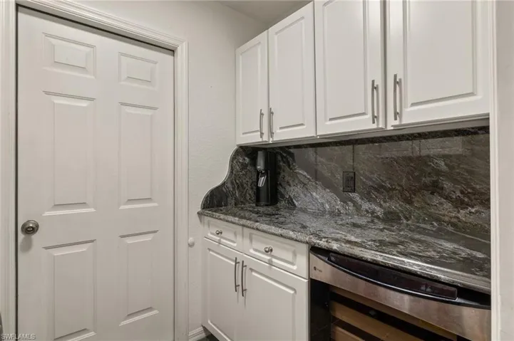 Kitchen with white cabinets, stone counters, beverage cooler, and tasteful backsplash
