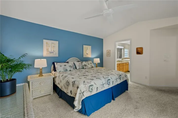 Carpeted bedroom featuring ceiling fan, lofted ceiling, and ensuite bathroom