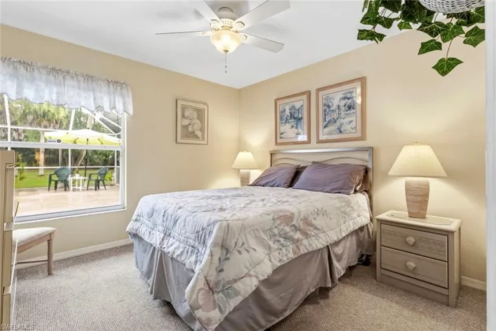 Carpeted room with a ceiling fan and a window overlooking a paved patio and lush landscaping