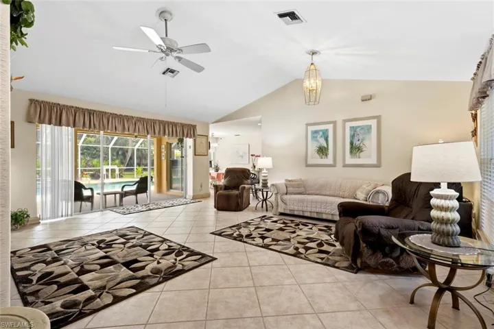 Expansive living area featuring vaulted ceilings, light tile flooring, and sliding glass doors opening to a screened-in pool enclosure, perfect for the Florida lifestyle of indoor/outdoor living.
