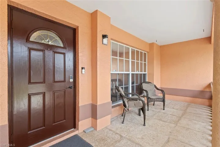 Covered entry with a dark wood-finish door featuring a decorative arched glass insert and a digital keypad lock