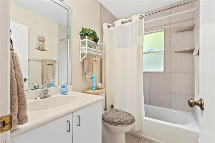 Second bathroom featuring a white vanity, a large wall-mounted mirror, full tub shower with built in shelving, and tile flooring