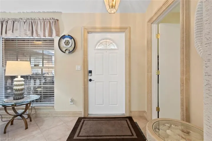 Entryway featuring a white paneled door with an arched glass insert, tile flooring, and a window with horizontal blinds