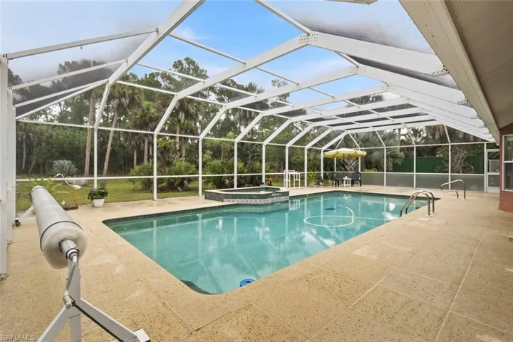 Screened-in outdoor pool area featuring a rectangular pool with a built-in spa.  Pool cover to the left.