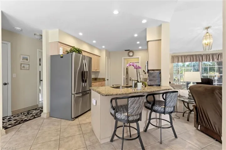 Kitchen featuring tile flooring, recessed lighting, stainless steel refrigerator, light wood cabinetry, and a granite countertop with an integrated sink