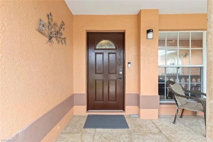 Entryway featuring a paneled front door with an arched glass insert, textured stucco walls, and large gridded windows