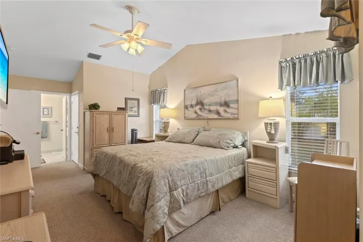 Master bedroom with vaulted ceilings elevate this carpeted room featuring a ceiling fan with integrated lighting, a window with horizontal blinds, and a private entrance to a bathroom with tile flooring