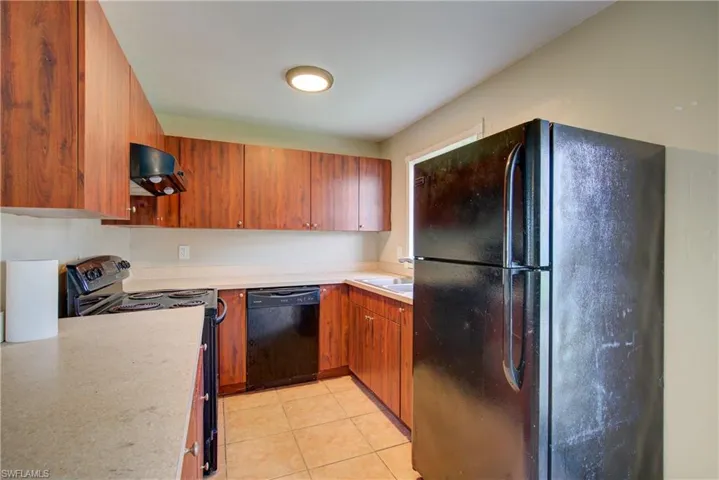Kitchen featuring black appliances, brown cabinets, range hood, and light tile patterned flooring