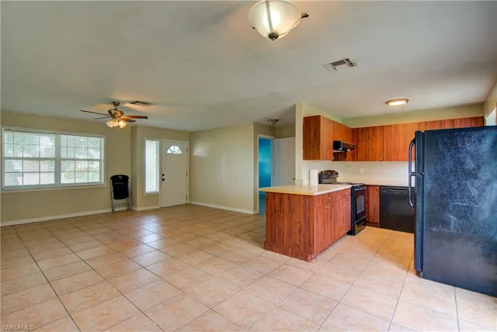 Kitchen featuring brown cabinets, light countertops, black appliances, a peninsula, and light tile patterned flooring