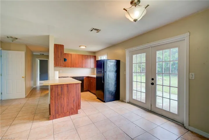 Kitchen with brown cabinets, light countertops, black appliances, a peninsula, and light tile patterned floors