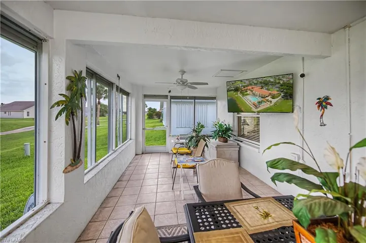 Screened lanai featuring tiled flooring, multiple windows, a ceiling fan, and built-in wall-mounted television