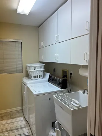 Dedicated laundry area featuring abundant white cabinetry, a utility sink, and tiled flooring