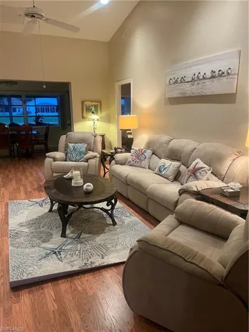 Spacious living area featuring vaulted ceilings, wood-finish flooring, and an expansive doorway leading to an additional space
