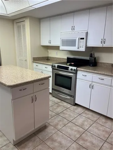 Kitchen featuring white cabinetry, light-toned stone-finish countertops, stainless steel range, and an over-the-range microwave