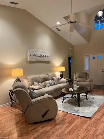 Living area featuring wood-finish flooring, a vaulted ceiling, and a ceiling fan with integrated lighting