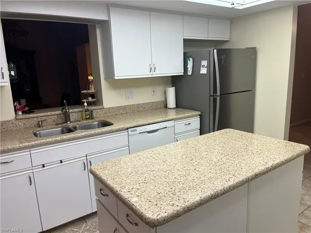 Kitchen featuring light-toned speckled countertops, white cabinetry with silver-tone hardware, a double-basin stainless steel sink, and a built-in dishwasher