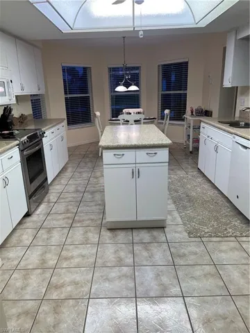 Kitchen featuring a central island with a light-toned countertop, white cabinetry, tile flooring, and multiple windows