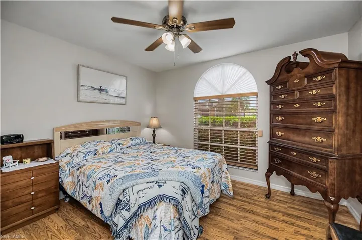 Bedroom featuring wood-finish flooring, a ceiling fan with integrated lighting, and a window with arched transom and horizontal blinds