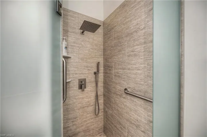 Walk-in shower featuring large format natural stone-look tiling, a rain showerhead, and a handheld shower sprayer