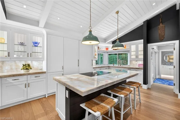 Kitchen with white cabinetry, glass insert cabinets, and lofted ceiling with beams