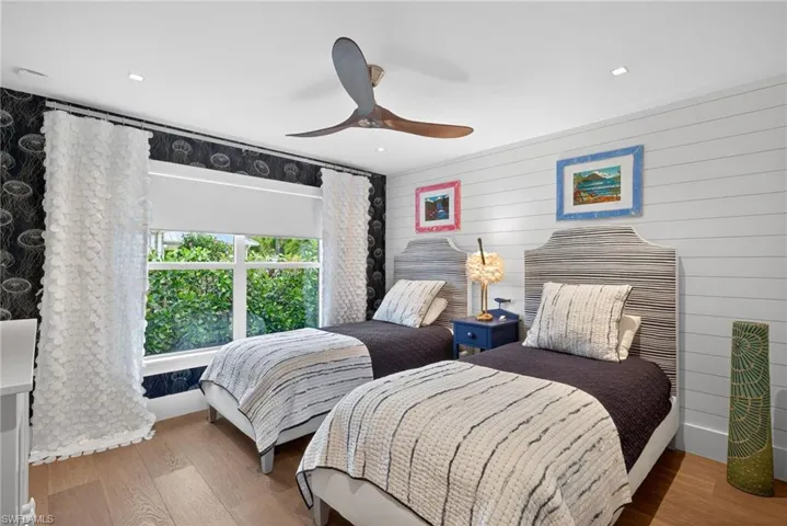 Bedroom featuring ceiling fan, light wood-style floors, and wooden walls